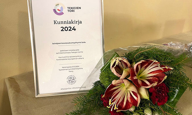 Kunniakirja kehyksissä ja kukkakimppu pöydällä kunniakirjan vieressä